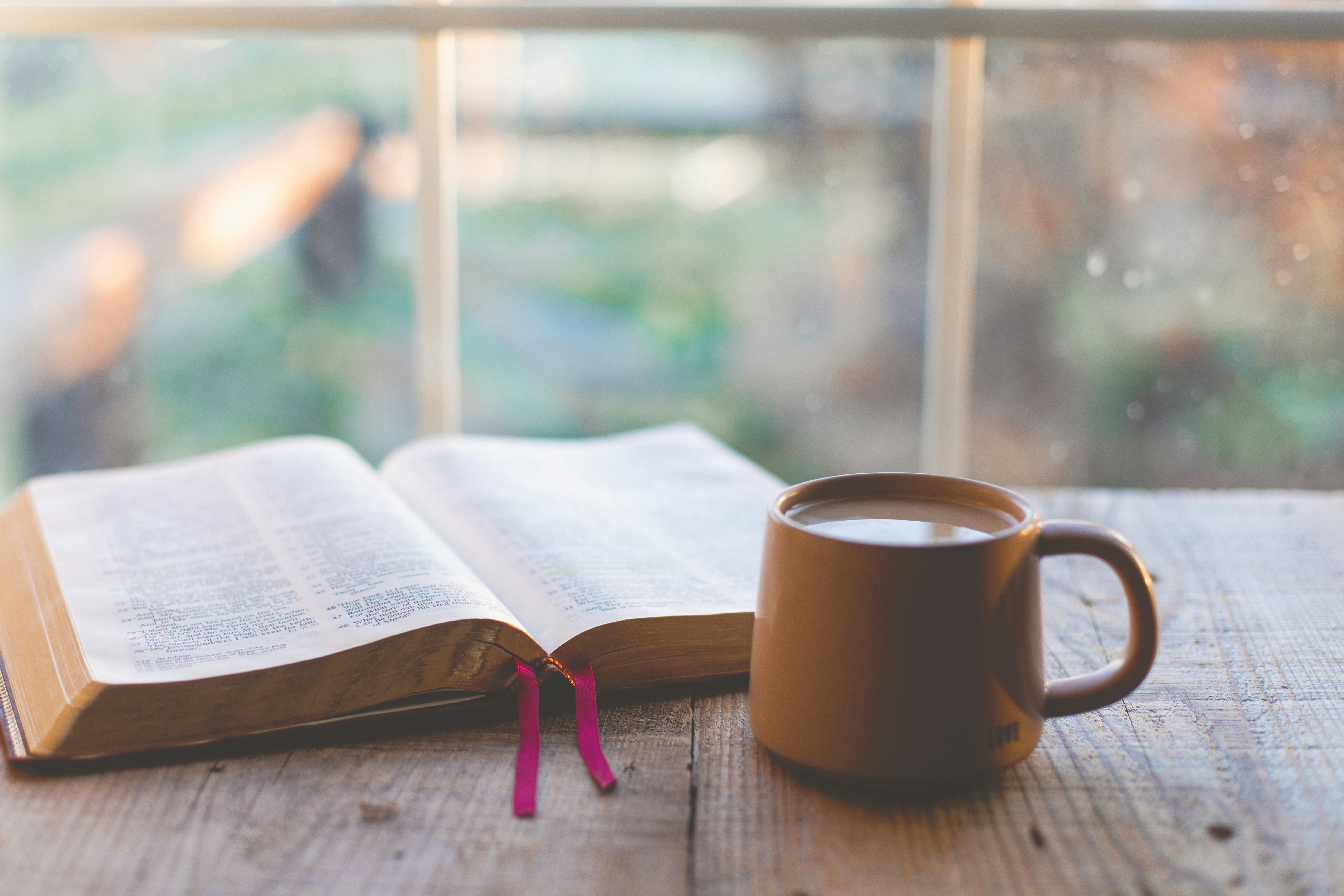 หนังสือเปิดอยู่บนโต๊ะไม้ข้างแก้วกาแฟริมหน้าต่างในแสงเช้า
