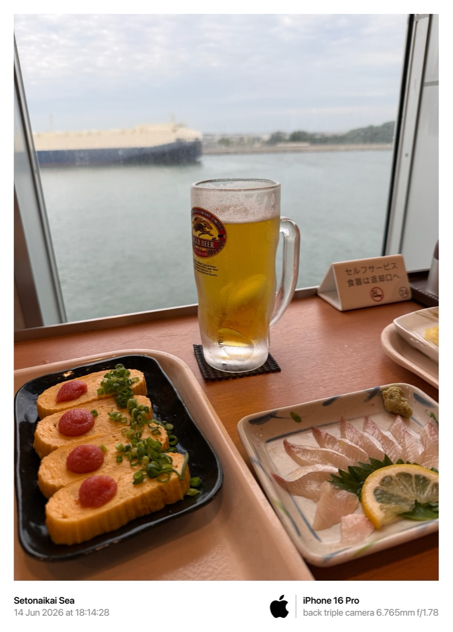 เบียร์เย็น ไข่ม้วน และปลาดิบวางอยู่ริมหน้าต่างเรือ โดยมีทะเลและท่าเรืออยู่ด้านนอก